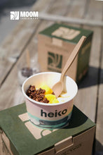 Charger l&#39;image dans la galerie, Dessert in a cup with a wooden spoon next to eco-friendly packaging by Heiko on a wooden table.