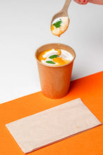 Load image into Gallery viewer, Cuillère réutilisable en canne à sucre soulevant une soupe crémeuse d&#39;un gobelet en kraft sur fond orange.