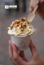 Charger l&#39;image dans la galerie, Main holding a cup of ice cream topped with crumbs, using a biodegradable sugar cane spoon.