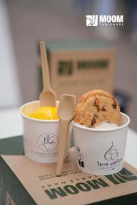 Cuillères à glace biosourcée en canne à sucre utilisées pour servir des glaces dans des pots, avec un cookie sur le dessus.