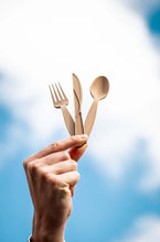 Charger l&#39;image dans la galerie, Hand holding biodegradable fork, knife, and spoon against a blue sky backdrop.