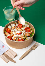 Cargar imagen en el visor de la galería, hand drizzling dressing on a salad with wooden cutlery in a biodegradable bowl on a colorful background.